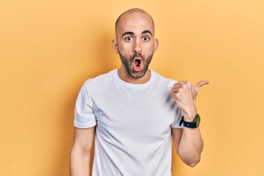Gündelik beyaz t-shirt giyen genç kel bir adam elleri yana doğru işaret ederek şaşırdı, ağzı açık hayret içinde kaldı.. 