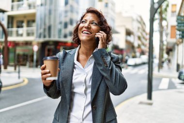 Orta yaşlı Latin iş kadını kahve içiyor ve şehirdeki akıllı telefondan konuşuyor..