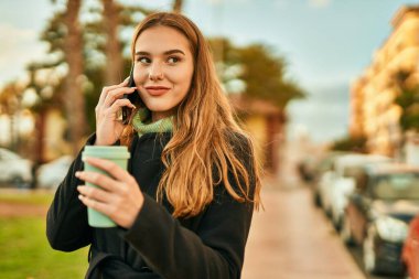 Genç sarışın kız akıllı telefondan konuşuyor. Şehirde kahve içiyor..