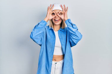 Yün şapka takan güzel sarışın kadın dürbün gibi jest yapıyor. Dürbün dilini çıkarıyor, gözler parmaklarından bakıyor. çılgın ifade. 