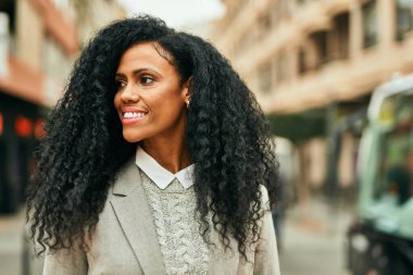 Orta yaşlı Afro-Amerikan iş kadını şehirde mutlu bir şekilde dikilirken gülümsüyor.