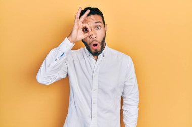 Sakallı, iş gömleği giyen İspanyol bir adam. Şaşırmış yüz ifadesiyle şaşırmış, parmaklarından bakan bir jest yapıyor. İnançsız ifade. 