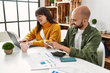 Genç İspanyol çift evde masada dizüstü bilgisayar kullanarak mutlu bir şekilde gülümsüyor..