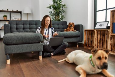 Genç İspanyol kadın evde köpeklerle yerde otururken görüntülü konuşma yapıyor.