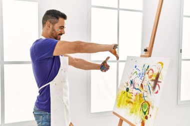 İspanyol asıllı genç adam kendine güvenen bir tablo çiziyor. Resim stüdyosunda elleriyle jest yapıyor.