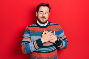 Handsome caucasian man with beard wearing elegant wool winter sweater smiling with hands on chest with closed eyes and grateful gesture on face. health concept. 