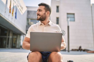 Sokakta dizüstü bilgisayar kullanarak gülümseyen İspanyol genç adam.