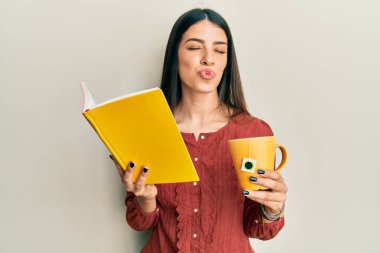 Genç İspanyol kadın kitap okuyor. Bir fincan çay içiyor. Kameraya bakıyor. aşk ifadesi. 