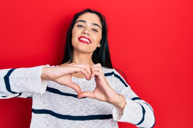 Gündelik kıyafetler giyen, aşık gülümseyen, elleriyle kalp sembolü yapan genç İspanyol kız. romantik kavram. 