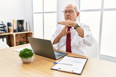 Senior man working at the office using computer laptop doing time out gesture with hands, frustrated and serious face 