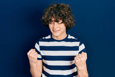 Handsome young man wearing casual striped t shirt very happy and excited doing winner gesture with arms raised, smiling and screaming for success. celebration concept. 