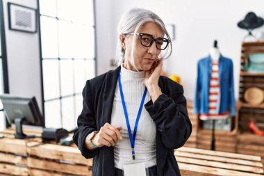 Perakende mağazasında yönetici olarak çalışan orta yaşlı, kır saçlı bir kadın diş ağrısı ya da diş ağrısı yüzünden ağızlarına acı dolu bir ifadeyle dokunuyor. dişçi 