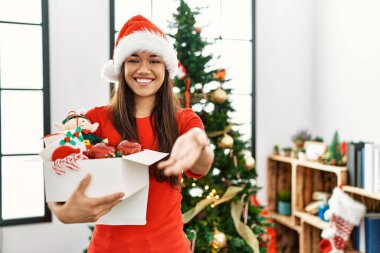 Genç esmer kadın Noel ağacının yanında elinde süslemelerle neşeli gülümseyerek yardım eli uzatıyor ve kabul ediyor.. 