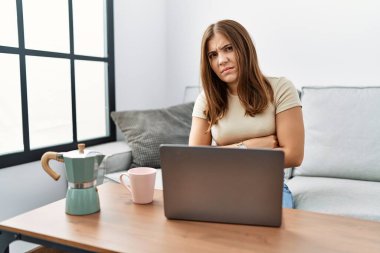 Genç esmer kadın evde dizüstü bilgisayar kullanıyor. Bir fincan kahve içiyor. Şüpheci ve gergin. negatif kişi. 