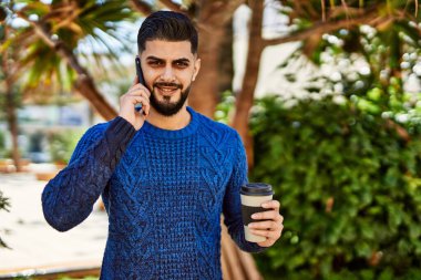 Genç Arap adam akıllı telefondan konuşuyor parkta kahve içiyor.