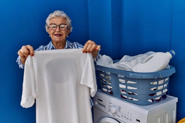 Starší Šedovlasá Žena Usmívá Sebevědomě Drží Bílé Tričko Prádelně — Stock fotografie