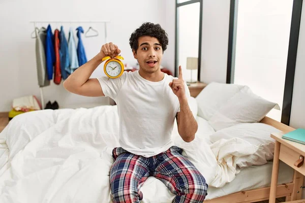 Junge Hispanische Mann Mit Wecker Sitzt Auf Dem Schlafzimmer Überrascht — Stockfoto