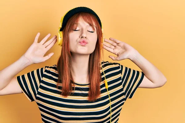 Redhead Young Woman Listening Music Using Headphones Looking Camera Blowing — Stockfoto