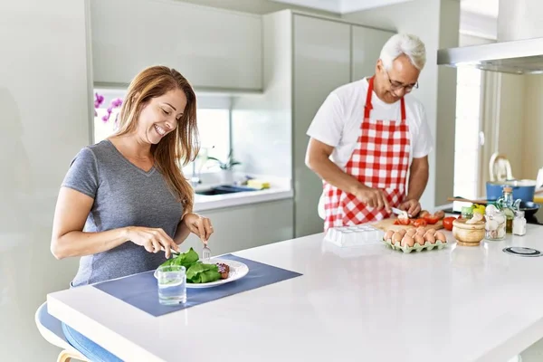中年惊慌失措的女人笑着吃沙拉 而男人则在厨房做饭 — 图库照片