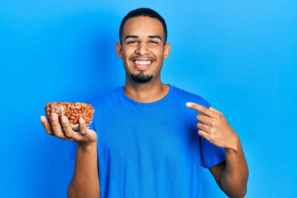 Joven Afroamericano Hombre Sosteniendo Tazón Cacahuetes Sonriendo Feliz Señalando Con — Foto de Stock
