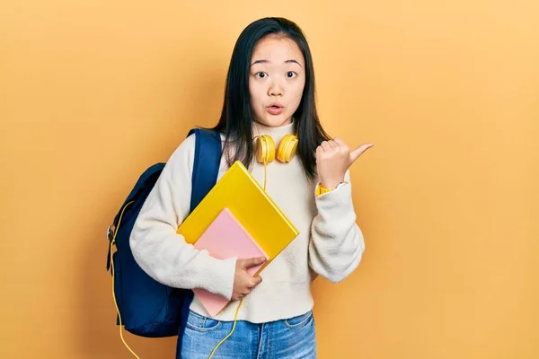 Young Chinese Girl Holding Student Backpack Books Surprised Pointing Hand — Stock Photo, Image