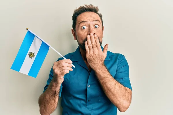 Hombre Mediana Edad Sosteniendo Bandera Argentina Cubriendo Boca Con Mano —  Fotos de Stock