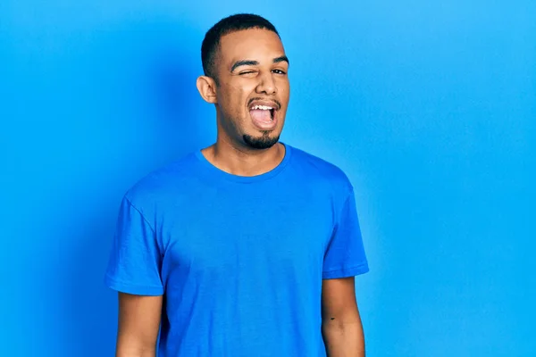 若いですアフリカ系アメリカ人男性身に着けていますカジュアルブルーTシャツウインク見ますザ カメラとともにセクシー表現 陽気で幸せな顔 — ストック写真