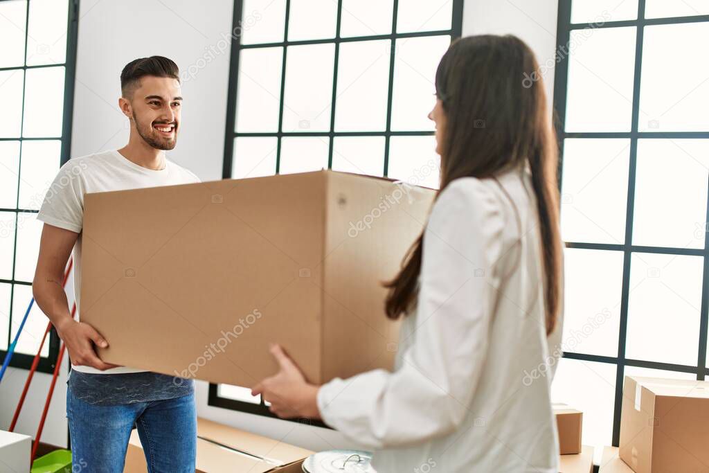 Young hispanic couple smiling happy holding cardboard boxes moving at new home.