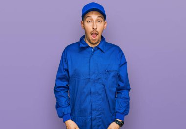 Bald man with beard wearing builder jumpsuit uniform afraid and shocked with surprise and amazed expression, fear and excited face. 