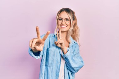 Gündelik kıyafetler ve gözlük takan güzel sarışın kadın kameraya bakıp zafer işareti yaparken parmaklarını gösteriyor. İki numara.. 