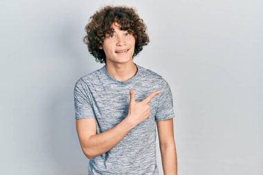 Handsome young man wearing casual grey t shirt smiling cheerful pointing with hand and finger up to the side 