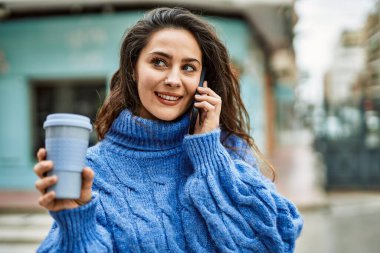 Genç İspanyol kadın akıllı telefondan konuşuyor ve şehirde kahve içiyor..