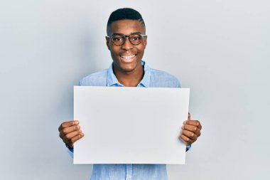 Gözlüklü, boş pankart taşıyan genç Afro-Amerikalı adam kahkahalarla gülüyor.. 