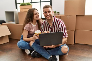 Kafkasyalı genç çift kahve içiyor ve yeni evlerinde dizüstü bilgisayar kullanıyorlar..