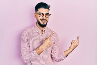 Sakallı, rahat gömlekli, gözlüklü, gülümseyen ve kameraya bakan yakışıklı bir adam.. 