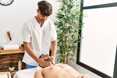 İki İspanyol erkek terapist ve hasta güzellik merkezinde yüz masajı yapıyorlar.