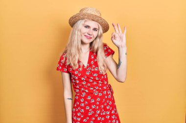 Sarı saçlı, yaz şapkalı, gülümseyen güzel beyaz kadın el ve parmaklarıyla tamam işareti yapıyor. başarılı ifade. 