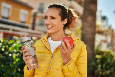 Genç İspanyol kız şehirde bir şişe su içip elma yiyor..