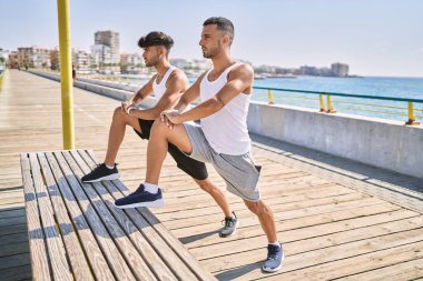 Two hispanic men couple stretching at seaside