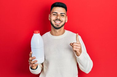 Sakallı, elinde litrelik süt şişesi olan genç İspanyol bir adam bir fikir veya soruyla gülümsüyor ve mutlu bir yüzle işaret ediyor. 