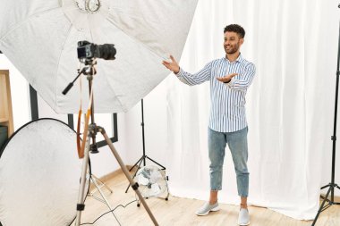 Arab young man posing as model at photography studio smiling cheerful offering hands giving assistance and acceptance. 