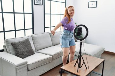 Genç kızıl saçlı kadın evde video dansı yapıyor.