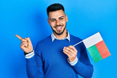 Sakallı genç İspanyol adam elinde madagaskar bayrağı Mutlulukla gülümsüyor 