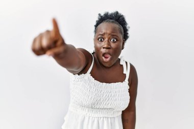 Genç Afrikalı bir kadın izole edilmiş beyaz arka planda duruyor. Parmağıyla işaret ediyor. İleriye şaşırmış, ağzı açık, şaşırmış bir ifade. 