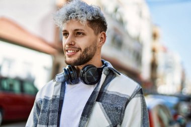 Şehirde kulaklık takarak mutlu gülümseyen genç İspanyol adam..