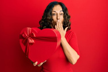 Orta yaşlı İspanyol bir kadın sevgililer günü hediyesini elinde tutuyor. Ağzını eliyle kapatıyor. Şok geçiriyor ve hata yapmaktan korkuyor. şaşırmış ifade 