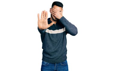 Sakallı, kışlık süveter giyen, elleriyle gözlerini kapatan, üzgün ve korku ifadeli İspanyol genç adam. utangaç ve olumsuz kavram. 