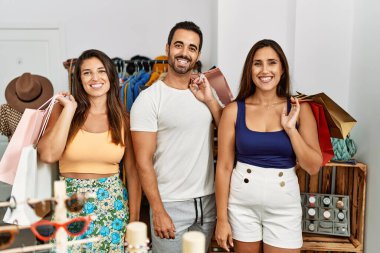 Giysi dükkanında alışveriş torbaları tutan bir grup İspanyol genç. Pozitif ve mutlu görünüyorlar. Dişlerini gösteren bir gülümsemeyle duruyorlar. 