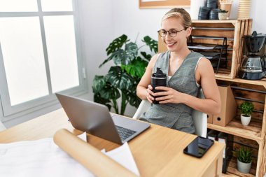 Genç beyaz kadın, kendine güvenen, kahve içen, mimarlık stüdyosunda çalışan, gülümseyen.