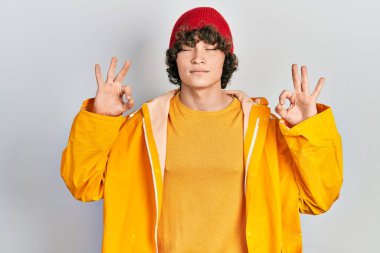 Handsome young man wearing yellow raincoat relax and smiling with eyes closed doing meditation gesture with fingers. yoga concept. 